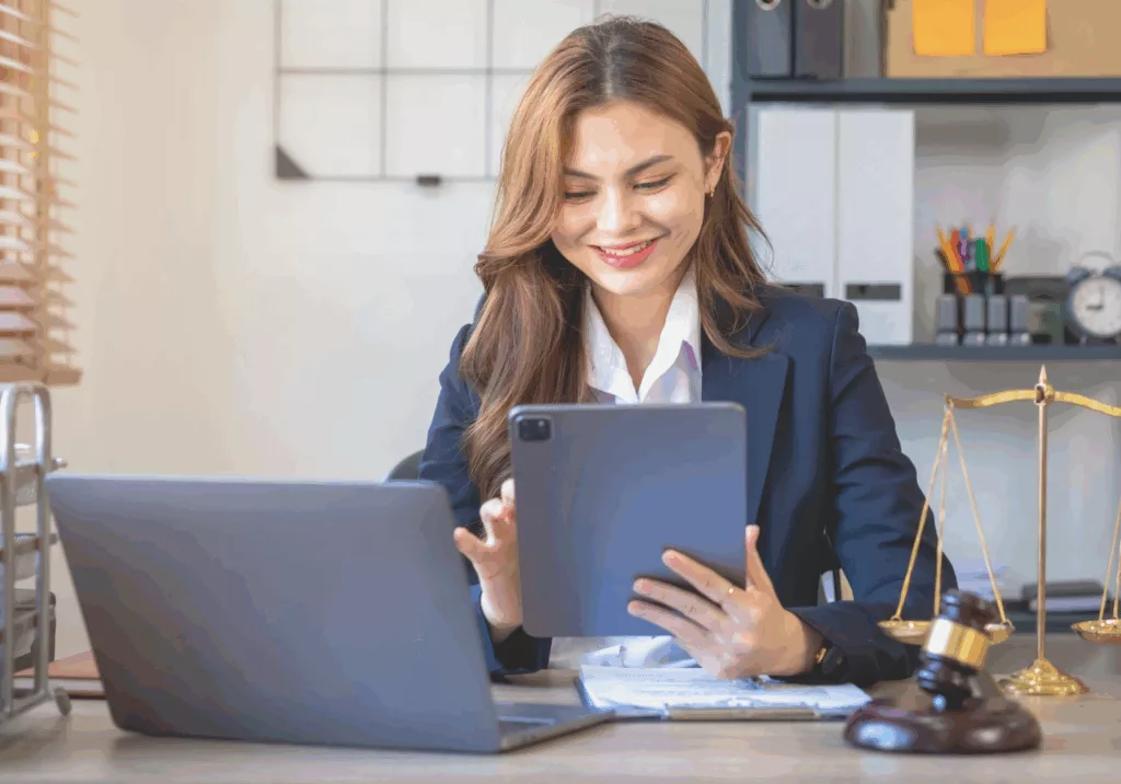 avocate souriant devant sa tablette et son ordinateur car son cabinet est bien organisé avec des outils juridiques